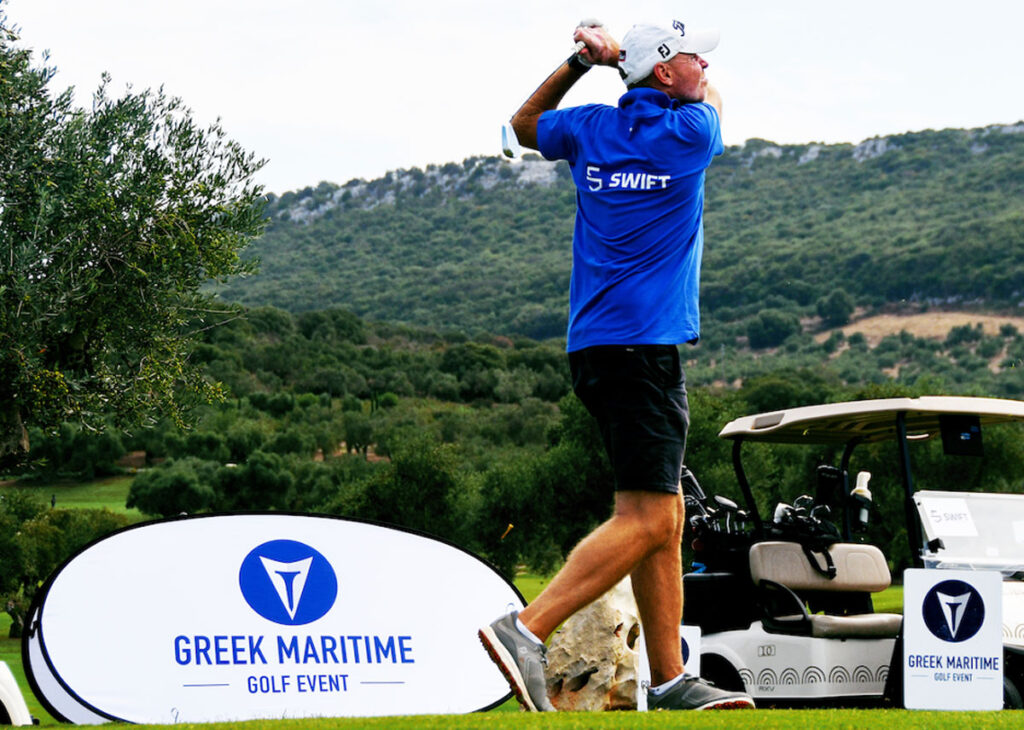 A man wearing a Swift Marine shirt swinging a golf club.